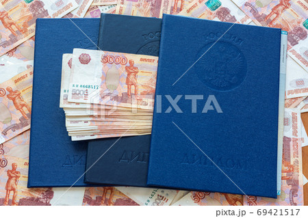 Three blue higher education diplomas lie in the background from the money, a bundle of money sticks out between the diplomas Three blue higher education diplomas lie in the background from the money, a bundle of money sticks out between the diplomas 69421517