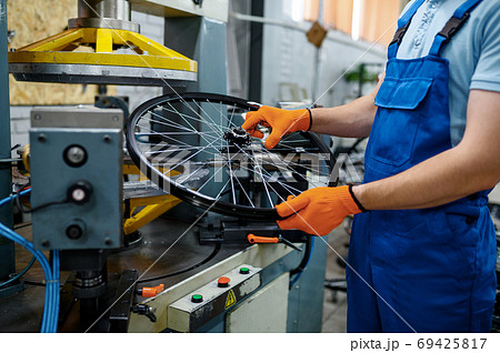 Mechanic holds bicycle wheel near machine tool 69425817