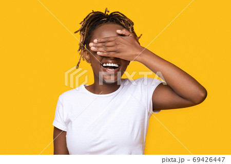 Happy black girl covering her eyes on yellow background Happy black girl covering her eyes on yellow background 69426447