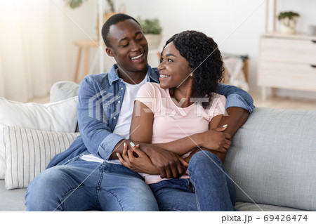 Happy african couple cuddling on sofa at home Happy african couple cuddling on sofa at home 69426474