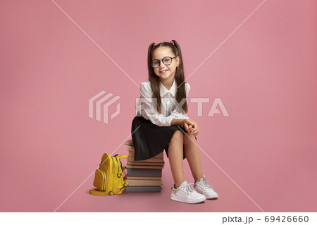 Elementary school education. Cheerful schoolgirl in glasses, sits on stack of books Elementary school education. Cheerful schoolgirl in glasses, sits on stack of books 69426660