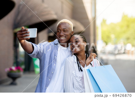 Modern fashion bloggers shopping. Smiling couple with bags hugging and making selfie for blog Modern fashion bloggers shopping. Smiling couple with bags hugging and making selfie for blog 69426870