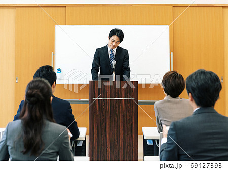 苦しい表情で講演をする男性 69427393
