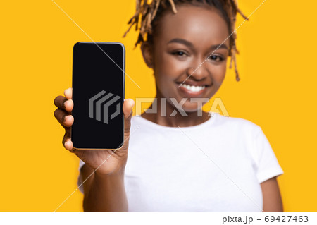Cheerful black girl showing smartphone with blank screen Cheerful black girl showing smartphone with blank screen 69427463