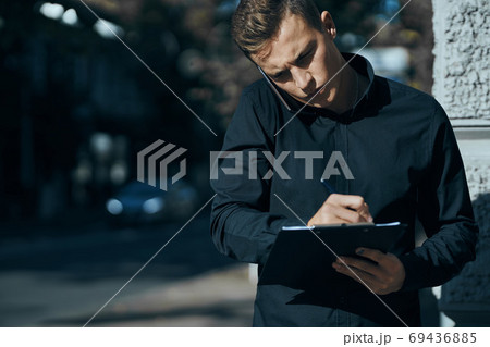 Business man in a shirt near the building with documents in his hands Business man in a shirt near the building with documents in his hands 69436885