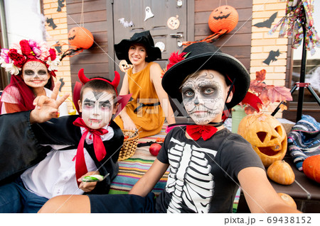 Two boys and girl with painted faces sitting on background of happy young woman 69438152