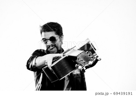A man plays the guitar in a black leather jacket with sunglasses on a light background 69439191
