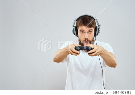 Man in headphones with gamepad playing hobby entertainment lifestyle light background Man in headphones with gamepad playing hobby entertainment lifestyle light background 69440395