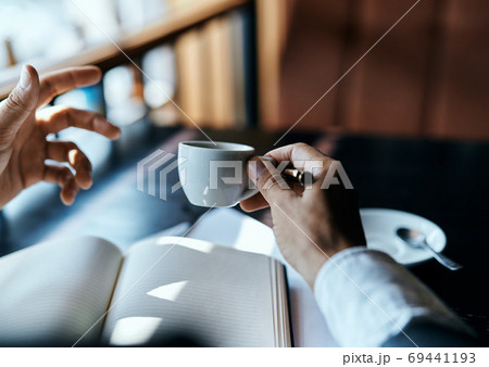 A man holds in his hand a cup of coffee pen books documents cafe A man holds in his hand a cup of coffee pen books documents cafe 69441193