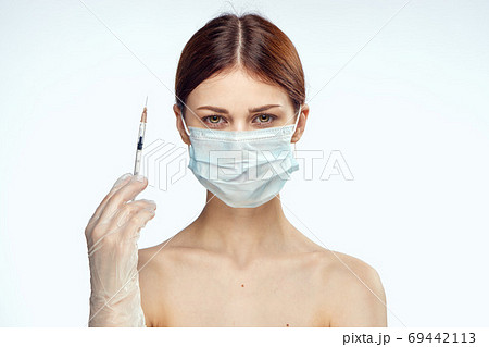 woman holding syringes in her hand injections medical mask naked shoulders rejuvenation light background 69442113