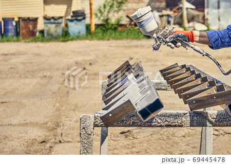 Crop man painting metal detail with paint gun in the backyard Crop man painting metal detail with paint gun in the backyard 69445478