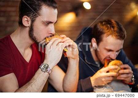 Two happy male friends eating tasty burgers in bar. 69447000