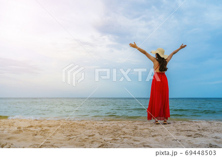 freedom woman in a red dress with arms raised on sea beach 69448503