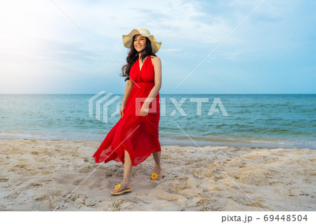 cheerful woman in red dress walking on sea beach 69448504