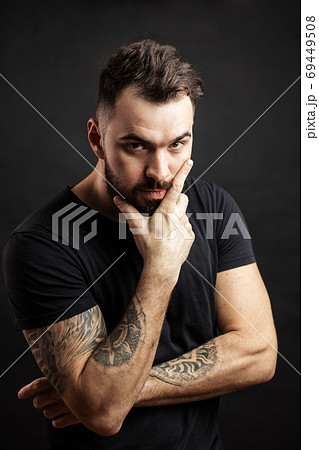 Strong man in black tight fitted shirt with a serious expression on his face. Strong man in black tight fitted shirt with a serious expression on his face. 69449508