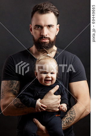 Handsome tattooed beared man holding cute little baby on black background 69449665