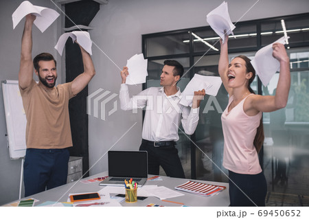 Excited female and two male coworkers laughing, tossing papers 69450652
