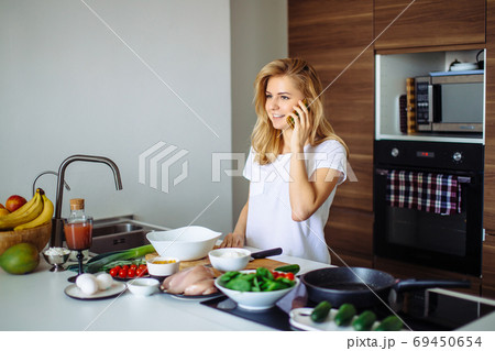 Caucasian woman making healthy meal and reading message at phone in kitchen. 69450654
