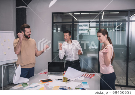 Excited female and two male coworkers tossing papers, happy with result Excited female and two male coworkers tossing papers, happy with result 69450655