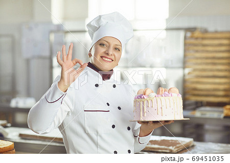 Confectioner is holding a cake in her hand in the bakery. 69451035