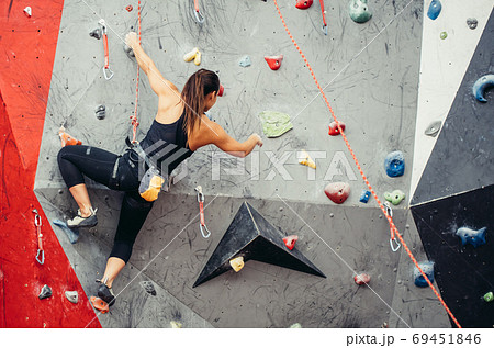 Fit sporty student girl moving up at rock climbing wall at the gym Fit sporty student girl moving up at rock climbing wall at the gym 69451846