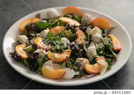 Closeup salad with nectarines, mozzarella and mixed greens in white plate on concrete background Closeup salad with nectarines, mozzarella and mixed greens in white plate on concrete background 69451980