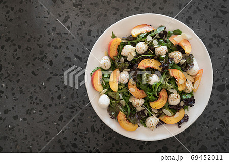 Top view of salad with nectarines, mozzarella and mixed greens in white plate on concrete background Top view of salad with nectarines, mozzarella and mixed greens in white plate on concrete background 69452011