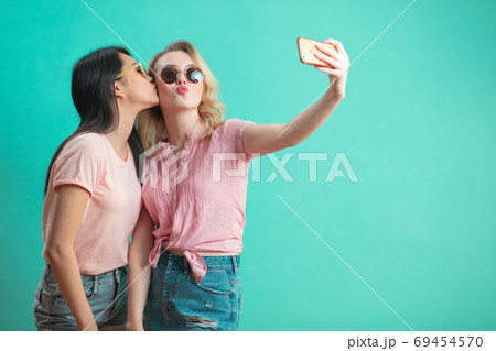 Diverse girls in casual outfits shooting selfie isolated on blue background. Diverse girls in casual outfits shooting selfie isolated on blue background. 69454570