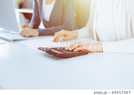 Accountant checking financial statement or counting by calculator income for tax form, hands close-up. Business woman sitting and working with colleague at the desk in office. Audit concept 69457487