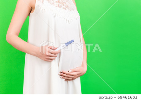 Cropped image of pregnant woman in white dress showing positive pregnancy test with two stripes at green background. Healthy pregnancy. Copy space 69461603