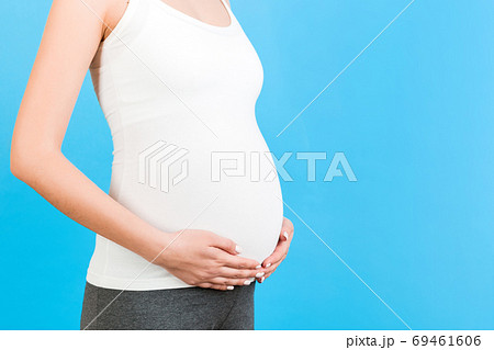 Close up of pregnant woman touching her abdomen at blue backgrou Close up of pregnant woman touching her abdomen at blue backgrou 69461606