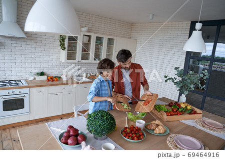 Cooking lunch with dad. Young father and his happy son preparing a salad while standing in the modern kitchen at home, spending time together 69464916
