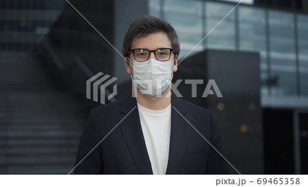 Businessman wearing mask looking at the camera, background of business buildings Businessman wearing mask looking at the camera, background of business buildings 69465358
