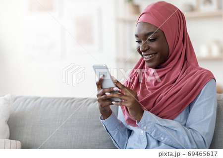 Happy black muslim woman in hijab using smartphone at home 69465617