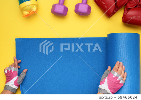 female hands in sports gloves unfold a sports mat on a yellow ba 69466024