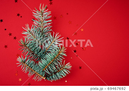 Christmas composition. Fir branches in a shape of christmas tree with festive confetti on red background with copy space 69467692