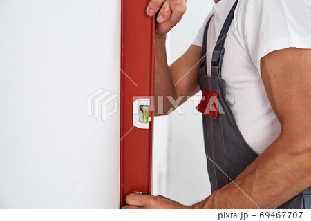 Renovation concept. Male worker checking level of the wall with the bubble level tool Renovation concept. Male worker checking level of the wall with the bubble level tool 69467707