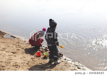 Two children are playing on the beach near the river. 69468685