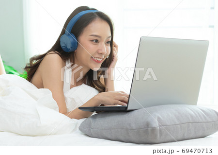 Asian woman working on a laptop sitting on the bed in the house. Asian woman working on a laptop sitting on the bed in the house. 69470713