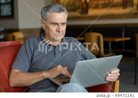 Handsome senior man using laptop and relaxing at home indoors Handsome senior man using laptop and relaxing at home indoors 69472281