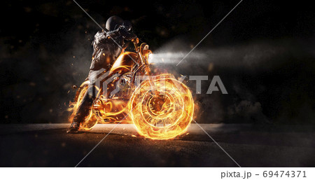 Dark motorbiker staying on burning motorcycle at night. 69474371