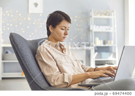 Businesswoman working on personal laptop sitting in comfortable armchair in cozy home office 69474400
