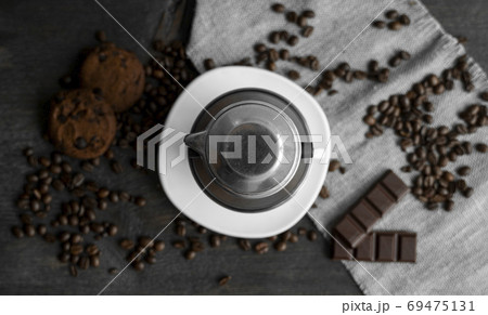 White cup of coffee with a metal filter on a top and scattered beans on a wooden table. Traditional vietnamese coffee. White cup of coffee with a metal filter on a top and scattered beans on a wooden table. Traditional vietnamese coffee. 69475131