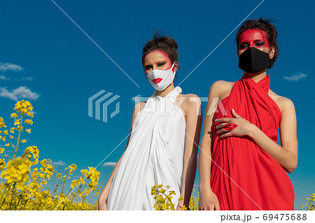 Two beautiful young brunette girls with creative bright makeup in tunics against a blue sky in a mask 69475688