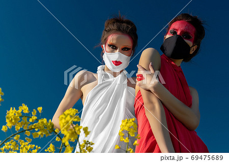 Two beautiful young brunette girls with creative bright makeup in tunics against a blue sky in a mask 69475689