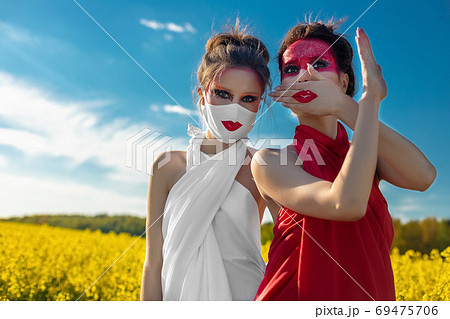 Two beautiful young brunette girls with creative bright makeup in tunics against a blue sky in a mask Two beautiful young brunette girls with creative bright makeup in tunics against a blue sky in a mask 69475706