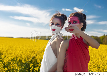 Two beautiful young brunette girls with creative bright makeup in tunics against a blue sky in a mask Two beautiful young brunette girls with creative bright makeup in tunics against a blue sky in a mask 69475707