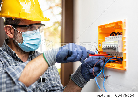 Electrician at work with face protected by surgical mask to prev Electrician at work with face protected by surgical mask to prev 69476054