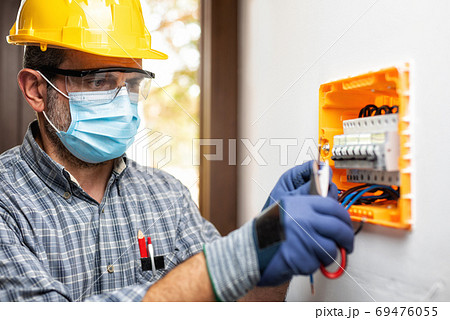 Electrician at work with face protected by surgical mask to prev Electrician at work with face protected by surgical mask to prev 69476055