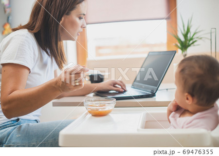 Funny adorable and dirty little baby girl of six months eats while sitting in the baby chair. 69476355